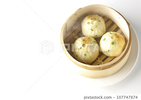 An overhead shot of piping hot xiaolongbao steamed in a steamer against a white background 107747874