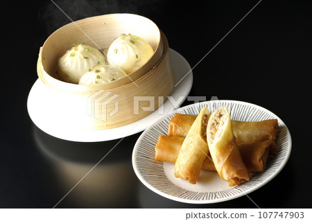 Fried spring rolls and piping hot xiao long bao in a steamer basket 107747903