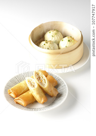 Fried spring rolls and piping hot xiao long bao in a steamer basket 107747917