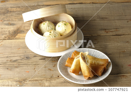 Fried spring rolls and piping hot xiao long bao in a steamer basket 107747921