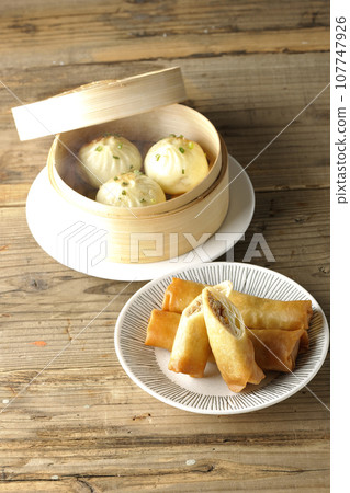 Fried spring rolls and piping hot xiao long bao in a steamer basket 107747926