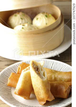 Fried spring rolls and piping hot xiao long bao in a steamer basket 107747929