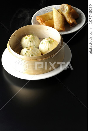 Piping hot xiaolongbao and fried spring rolls in a steamer basket 107748029