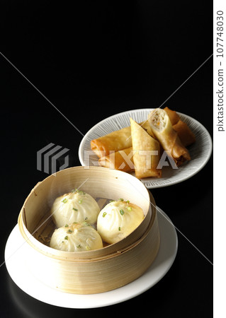 Piping hot xiaolongbao and fried spring rolls in a steamer basket 107748030