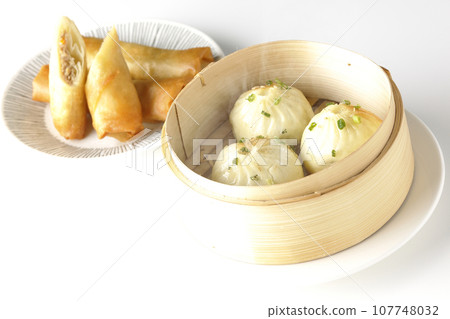 Piping hot xiaolongbao and fried spring rolls in a steamer basket 107748032