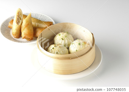 Piping hot xiaolongbao and fried spring rolls in a steamer basket 107748035