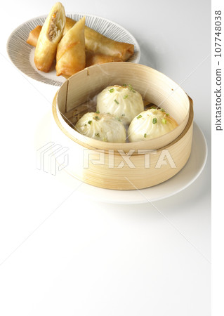 Piping hot xiaolongbao and fried spring rolls in a steamer basket 107748038
