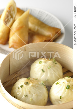 Piping hot xiaolongbao and fried spring rolls in a steamer basket 107748040