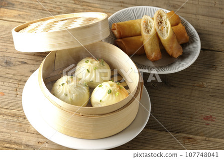 Piping hot xiaolongbao and fried spring rolls in a steamer basket 107748041
