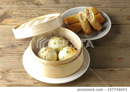 Piping hot xiaolongbao and fried spring rolls in a steamer basket 107748043