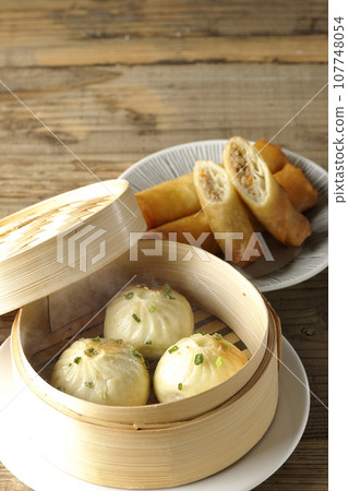 Piping hot xiaolongbao and fried spring rolls in a steamer basket 107748054