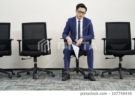 young male asian job seeker sitting in chair appears to be frustrated and defeated young male asian job seeker sitting in chair appears to be frustrated and defeated 107748436