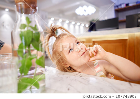Little kid waiting breakfast at cafe. Portrait of a adorable girl who makes faces at the camera. A walk with my parents on a day off. Little kid waiting breakfast at cafe. Portrait of a adorable girl who makes faces at the camera. A walk with my parents on a day off. 107748902