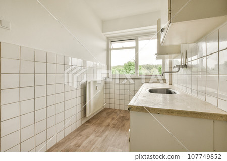 a kitchen with white tiles on the walls and wood flooring in front of the sink, there is an open window 107749852