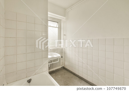 a bathroom with white tiles on the walls and floor, along with a bathtub in the corner of the room a bathroom with white tiles on the walls and floor, along with a bathtub in the corner of the room 107749870