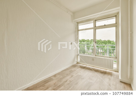 an empty room with wood flooring and white walls, looking out onto the balcony from the living room door 107749884