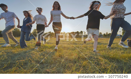 School friends running across the field holding hands at sunset. School friends running across the field holding hands at sunset. 107750240