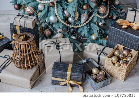 A variety of colored Christmas gifts stand near a decorative Christmas tree in the house on the floor under the branches. A variety of colored Christmas gifts stand near a decorative Christmas tree in the house on the floor under the branches. 107750835