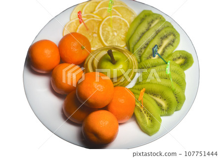 Fruit white plate with tangerines, kiwi, sliced apple and lemon slices on background isolated Fruit white plate with tangerines, kiwi, sliced apple and lemon slices on background isolated 107751444