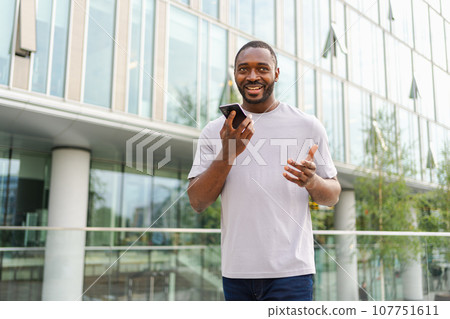 African american man talking on smartphone on street in city outdoor. Man with cell phone chatting with friends. Smiling person making answering call by cellphone. Guy having conversation by mobile African american man talking on smartphone on street in city outdoor. Man with cell phone chatting with friends. Smiling person making answering call by cellphone. Guy having conversation by mobile 107751611