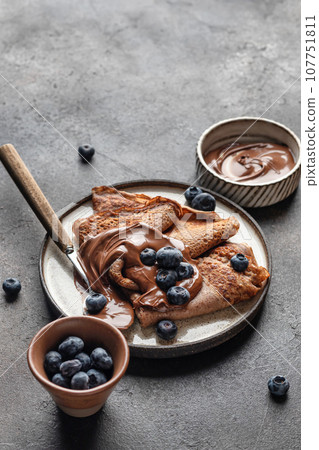 Chocolate crepes with blueberry and chocolate paste on brown textured background with text space 107751811