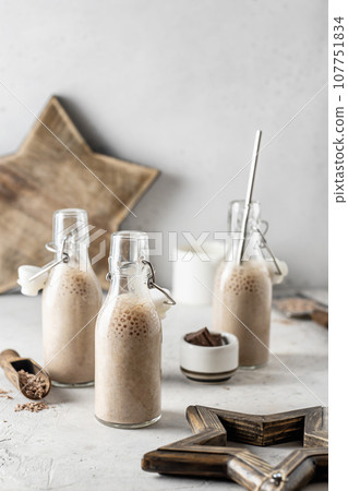 Chocolate milkshakes in glass bottles with christmas decoration woodem stars on gray background. Christmas mood, festive xmas still life 107751834