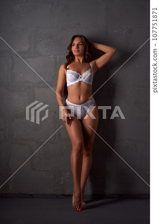 Alluring woman in lace lingerie standing against gray wall 107751871