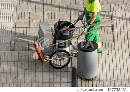 Sweeper worker pushing a cart on a city sidewalk Sweeper worker pushing a cart on a city sidewalk 107752481