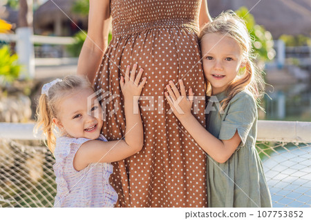 Sisters' love blooms as they tenderly embrace their mother's pregnant belly, sharing anticipation and affection for their soon-to-arrive sibling Sisters' love blooms as they tenderly embrace their mother's pregnant belly, sharing anticipation and affection for their soon-to-arrive sibling 107753852