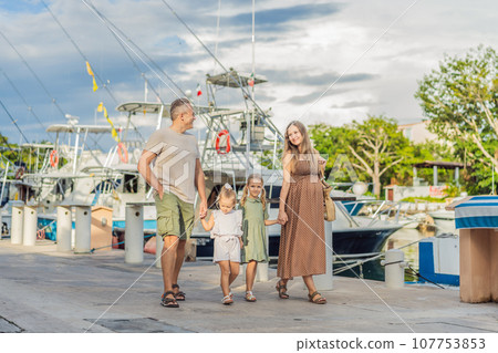 A happy, mature couple over 40 with their two daughters enjoying a leisurely walk on the waterfront, their joy evident as they embrace the journey of pregnancy later in life 107753853