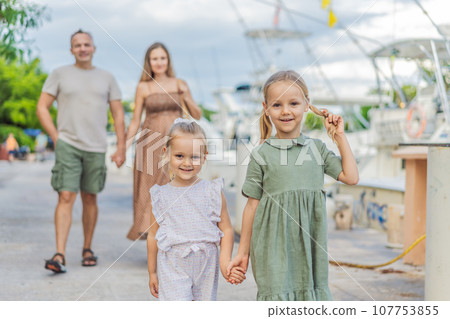 A happy, mature couple over 40 with their two daughters enjoying a leisurely walk on the waterfront, their joy evident as they embrace the journey of pregnancy later in life 107753855