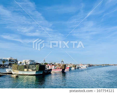Canal de Tavira . Small boat cruising tranquil green river. 107754121
