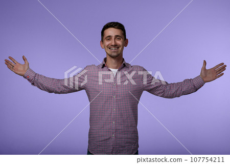 Portrait of young happy man with braces smiling with hands raised to the sides. Successful happy man on purple background. Portrait of young happy man with braces smiling with hands raised to the sides. Successful happy man on purple background. 107754211