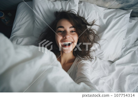 Happy young woman waking up in bed 107754314