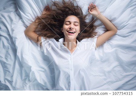 Happy young woman waking up in bed 107754315