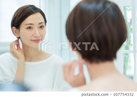 Woman putting on earrings in the makeup room Woman putting on earrings in the makeup room 107754332