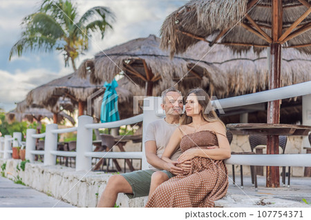 A happy, mature couple over 40, enjoying a leisurely walk in a park, their joy evident as they embrace the journey of pregnancy later in life A happy, mature couple over 40, enjoying a leisurely walk in a park, their joy evident as they embrace the journey of pregnancy later in life 107754371