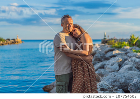 A happy, mature couple over 40, enjoying a leisurely walk on the waterfront On the Sunset, their joy evident as they embrace the journey of pregnancy later in life A happy, mature couple over 40, enjoying a leisurely walk on the waterfront On the Sunset, their joy evident as they embrace the journey of pregnancy later in life 107754502