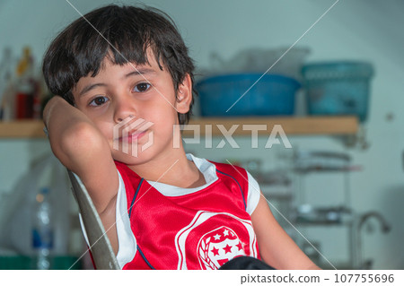 A boy wear red shirt sitting in the kitchen during waiting for a meal A boy wear red shirt sitting in the kitchen during waiting for a meal 107755696