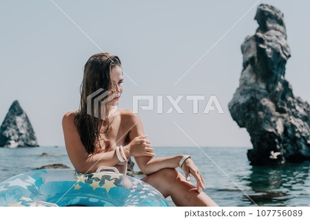 Woman summer sea. Happy woman swimming with inflatable donut on the beach in summer sunny day, surrounded by volcanic mountains. Summer vacation concept. Woman summer sea. Happy woman swimming with inflatable donut on the beach in summer sunny day, surrounded by volcanic mountains. Summer vacation concept. 107756089