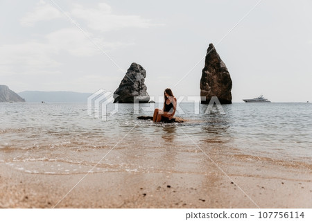 Woman summer travel sea. Happy tourist enjoy taking picture outdoors for memories. Woman traveler posing on the beach at sea surrounded by volcanic mountains, sharing travel adventure journey 107756114