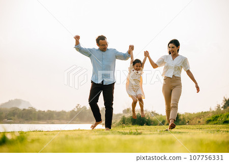 Happy family running through a beautiful green field on a sunny summer day, enjoying the freedom and beauty of nature together, Happy Family Day Concept 107756331