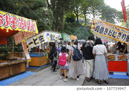 A photo of the stalls at the festival. Overflowing people gathered at the open air for the fair. Enjoying food while listening to festival music 107759947
