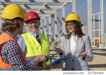 Smiling Female Architect, Mature Businessman and Construction Foreman Meeting at Construction Site 107760409