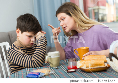 Upset mother and unhappy son arguing during breakfast indoors Upset mother and unhappy son arguing during breakfast indoors 107761227