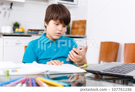 Boy using phone while doing homework 107761286