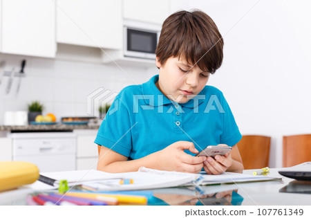 Boy using phone while doing homework Boy using phone while doing homework 107761349