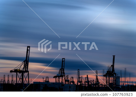 Sunset Over Busy Commercial Port with Silhouette of Massive Cranes Sunset Over Busy Commercial Port with Silhouette of Massive Cranes 107763923