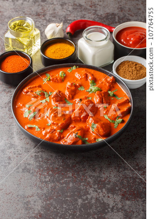 Chicken tikka masala traditional dish of indian cuisine in a black bowl with ingredients over dark concrete background. Vertical 107764755