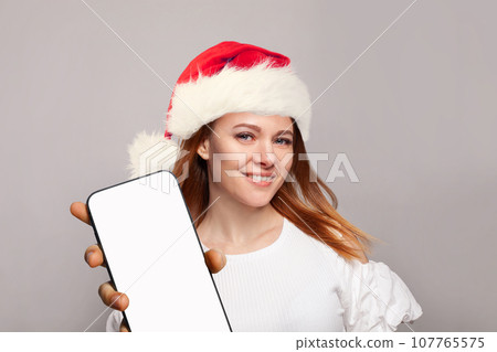 Christmas portrait of perfect  woman in red Santa hat showing smartphone display 107765575